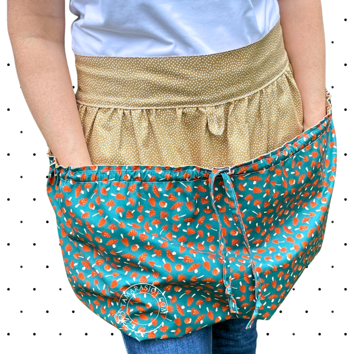 Person wearing a gold apron over a white shirt with a teal apron pocket featuring orange patterns.